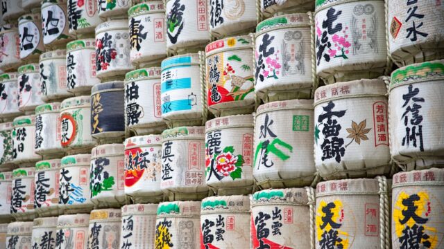 神社に奉納された色とりどりの菰樽(こもだる)が積み重なった壁。各蔵元の銘柄名が書かれたラベルが並んでいる