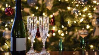 クリスマスツリーの前に置かれたスパークリングワインのボトルとグラス2脚。年末年始の乾杯シーンを表す写真