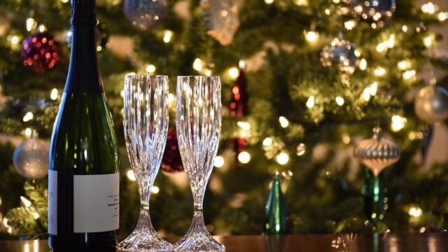 クリスマスツリーの前に置かれたスパークリングワインのボトルとグラス2脚。年末年始の乾杯シーンを表す写真