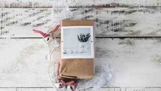 クリスマス飾りと共に木の床に置かれた茶色いラッピングの小包。年末の贈り物・発送をイメージした写真