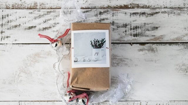 クリスマス飾りと共に木の床に置かれた茶色いラッピングの小包。年末の贈り物・発送をイメージした写真
