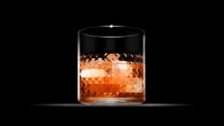 暗い背景に照らされた琥珀色の洋酒グラス、氷入り。焼酎のロック飲みをイメージした写真