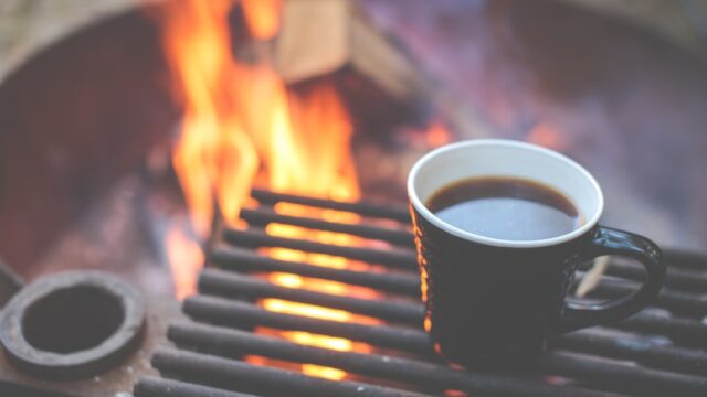焚き火の網の上で温かい飲み物が入ったマグカップを温めている様子