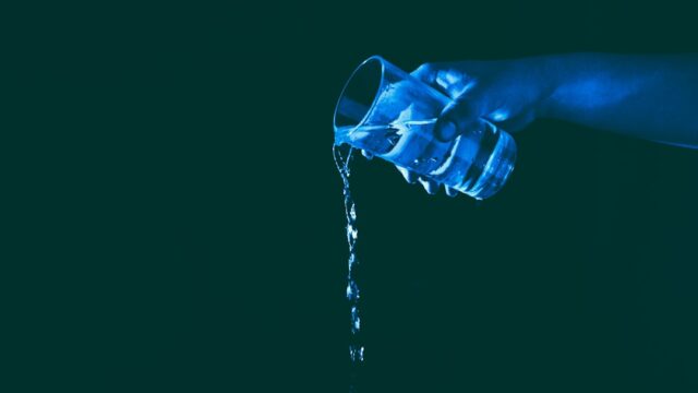 青みがかった照明の中グラスに液体を注ぐ手元